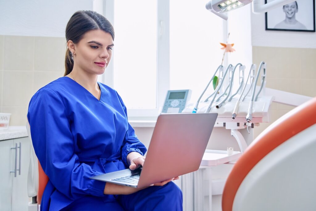 dentist on computer in office surrounded by dental tools