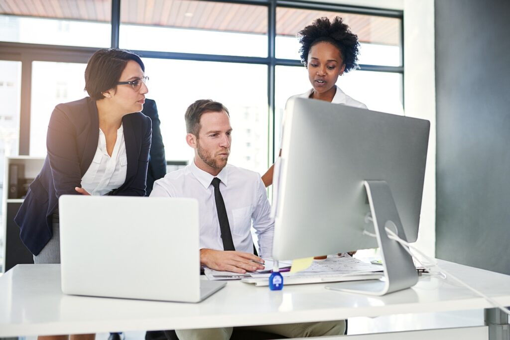 three coworkers working in office on computer and discussing work tasks