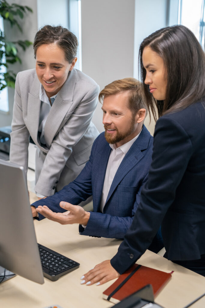 Three young office workers in suits at IT consulting company looking at computer screen during presentation